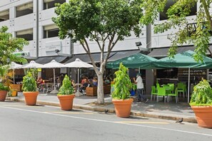 A street with outdoor seating, potted plants, and a building with signage. - Sun Drift Views | Modern in the Heart of Condado (San Juan)