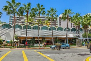 A hotel with a modern architectural design, featuring a white facade with arched windows and a series of palm trees in front. - Sun Drift Views | Modern in the Heart of Condado (San Juan)