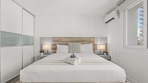 A modern hotel room with a large bed, two bedside tables with lamps, a wooden headboard, and a window with a city view. - Sun Drift Views | Modern in the Heart of Condado (San Juan)