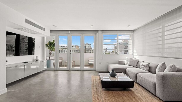 A modern living room with a grey sofa, a coffee table, and a TV on a white cabinet. - Sun Drift Views | Modern in the Heart of Condado (San Juan)