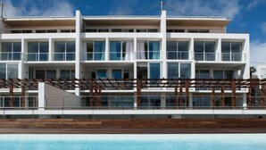 A modern hotel with a pool, featuring a multi-story structure with balconies and a wooden deck. - Boavista Apartment (Praia da Vitória)