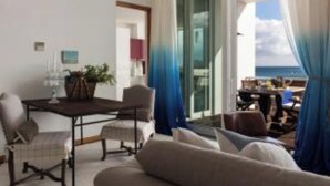 A room with a dining table, chairs, a sofa, and a view of the sea through large windows. - Boavista Apartment (Praia da Vitória)