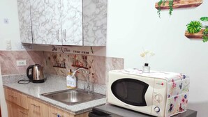Una cocina compacta con muebles de mármol, un lavamanos de acero inoxidable, un hervidor, un tostador y un refrigerador.