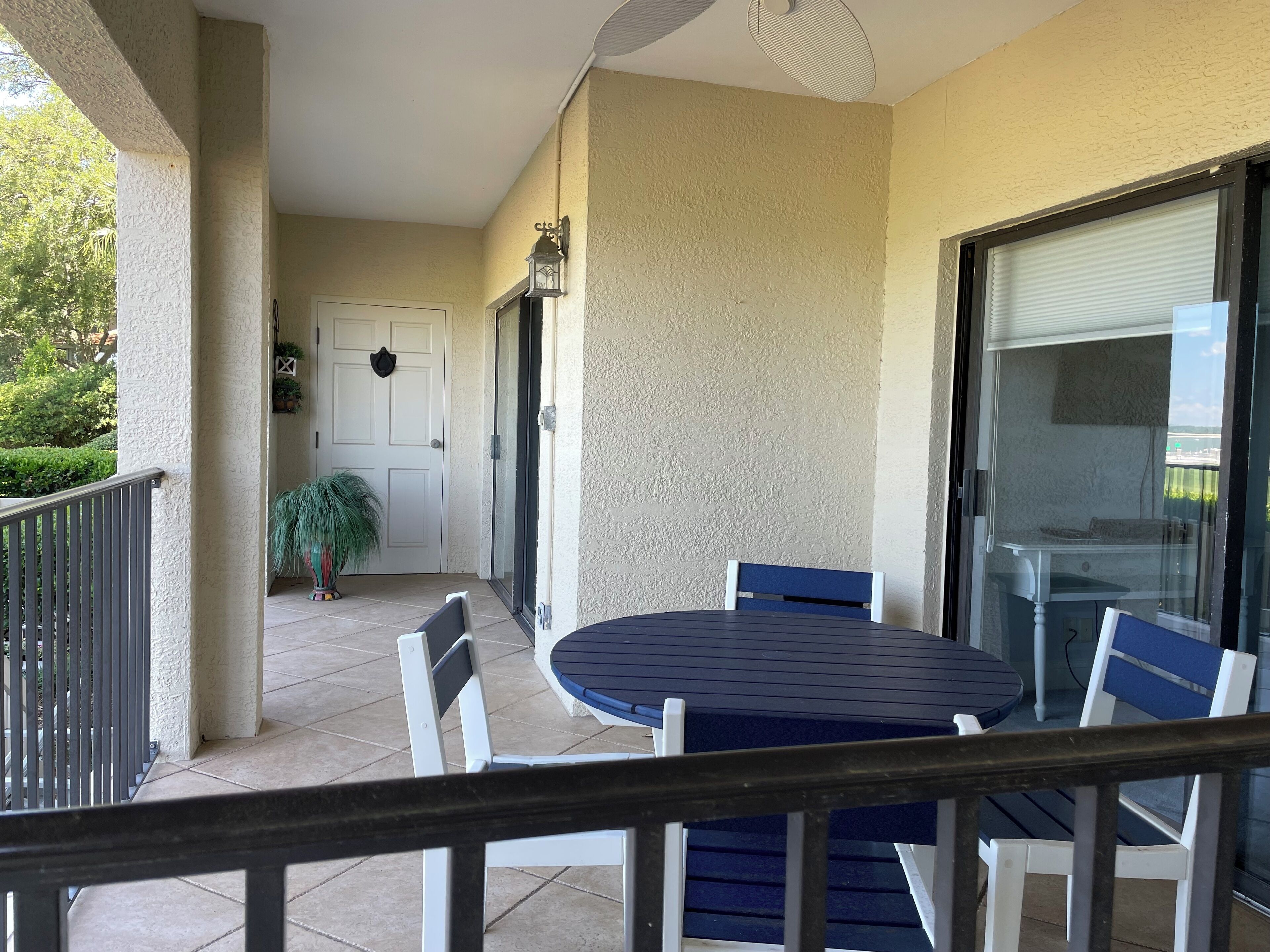 Um alpendre coberto com uma mesa redonda e cadeiras, uma porta com grinalda e vista para o verde.