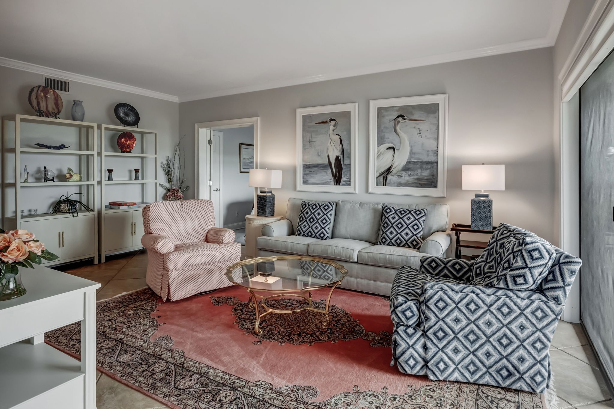 A modern living room with a sofa, armchair, and coffee table, featuring artwork and decorative items.