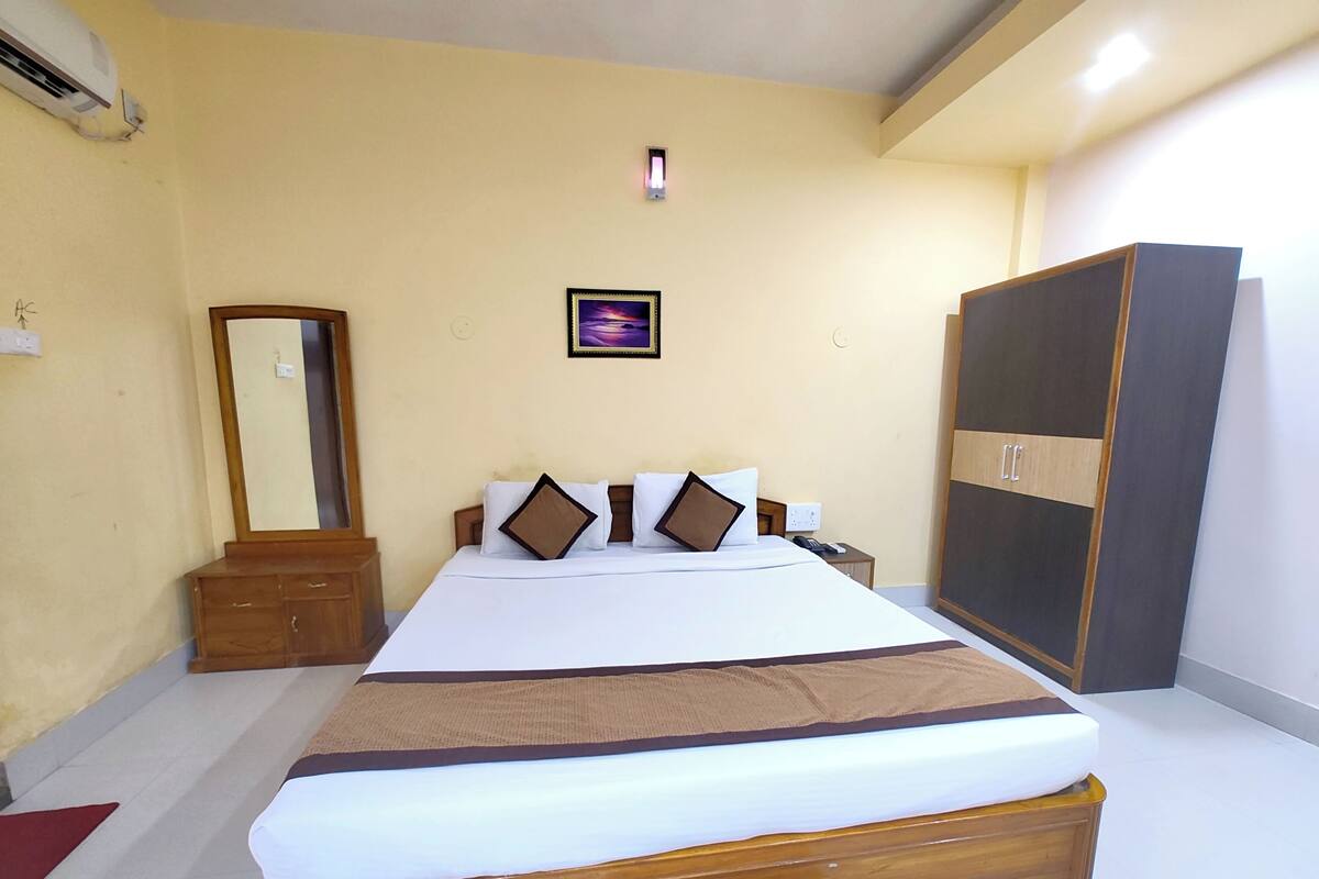 A hotel room with a large bed, a wardrobe, a mirror, and a small bedside table.