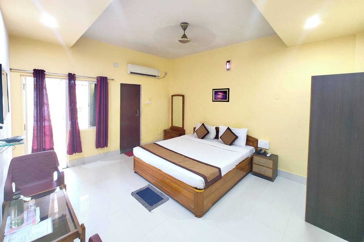 A hotel room with a bed, bedside table, nightstand, and a desk with a chair.