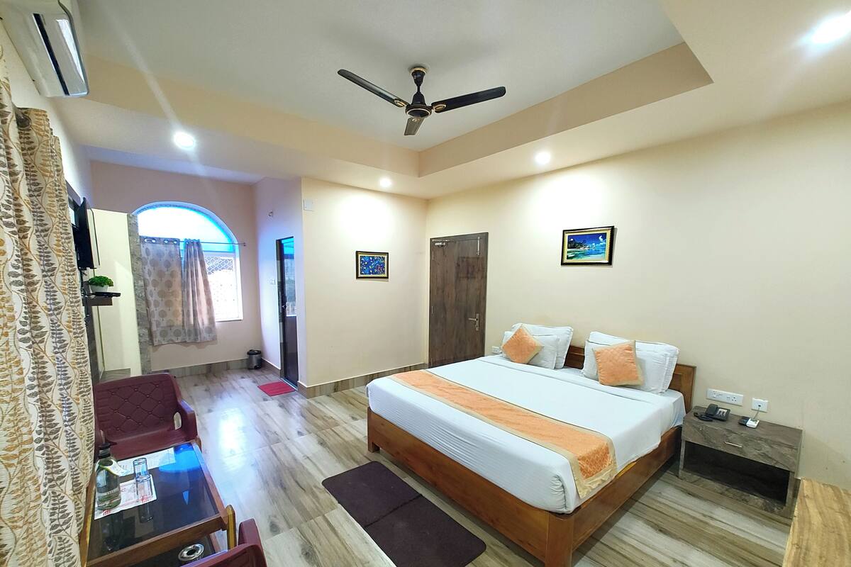 A hotel room with a bed, a desk, a chair, a ceiling fan, and a window with curtains.