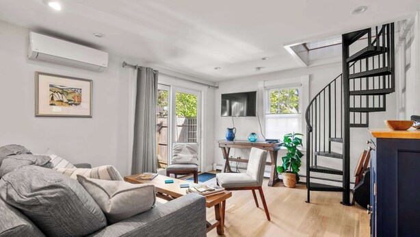 A modern living room with a sofa, a dining table, and a staircase. - Charming Getaway 1 Block from Beach! (Provincetown)