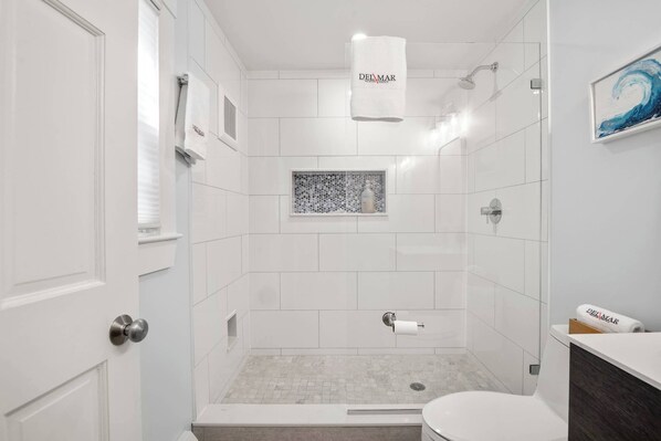 A modern bathroom with a shower, toilet, and a small window with a mosaic design.