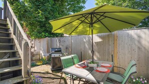 A backyard with a wooden fence, a grill, a dining table with chairs, and a yellow umbrella. - Charming Getaway 1 Block from Beach! (Provincetown)