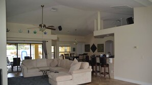 A spacious living room with a large sectional sofa, a dining area with a kitchen in the background, and a ceiling fan.