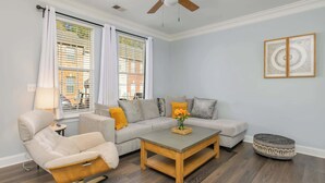 A modern living room with a sofa, armchair, coffee table, and a ceiling fan. - Cozy Corner Oasis (Cornelius)