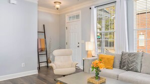 A living room with a sofa, a chair, a coffee table, a lamp, and a window with blinds. - Cozy Corner Oasis (Cornelius)
