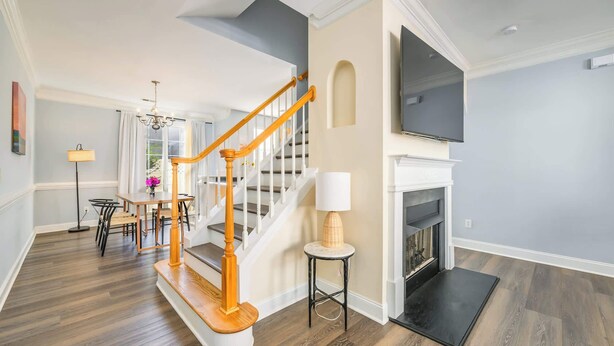 A spacious living room with a wooden staircase, a fireplace, and a flat-screen TV mounted above it. - Cozy Corner Oasis (Cornelius)