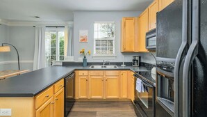 A modern kitchen with wooden cabinets, a black refrigerator, and a built-in oven. - Cozy Corner Oasis (Cornelius)