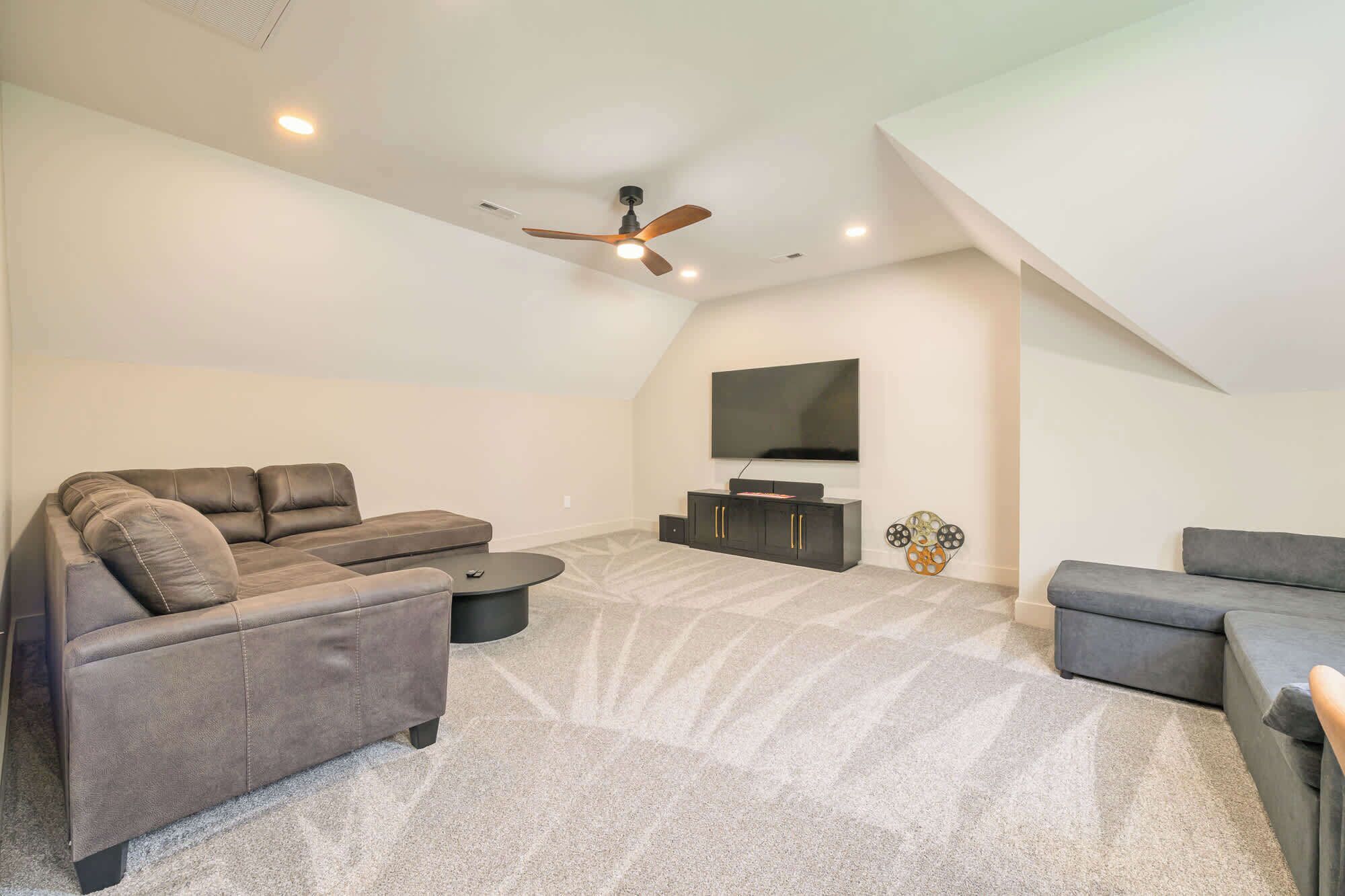 A modern living room with a sectional sofa, a coffee table, a flat-screen TV, and a ceiling fan.