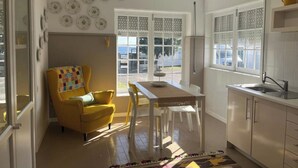 A bright kitchen with a dining area, a yellow armchair, and a view through the window. - Two Bedroom Apartment R C Porto Martins Pools (Porto Martins)