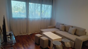 Una sala de estar moderna con un sofá, otomanas, una mesa de centro y un televisor sobre una mesa de vidrio.