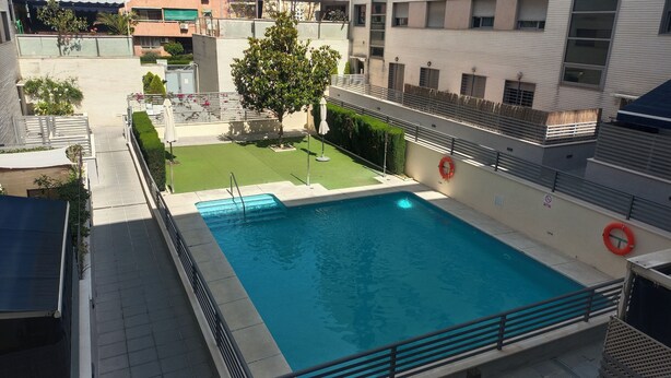 Una piscina con un flotador salvavidas, un área con césped y una cerca de metal.