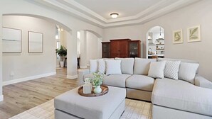 A spacious living room with a large L-shaped sectional sofa, a wooden cabinet, and a decorative tray on an ottoman. - Relaxing 3BAPool+Hot Tub Near the River & Wineries (Walnut Grove)