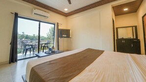 Habitación de hotel con cama, ventilador de techo, aire acondicionado, televisión, armario y balcón con sillas y una mesa.