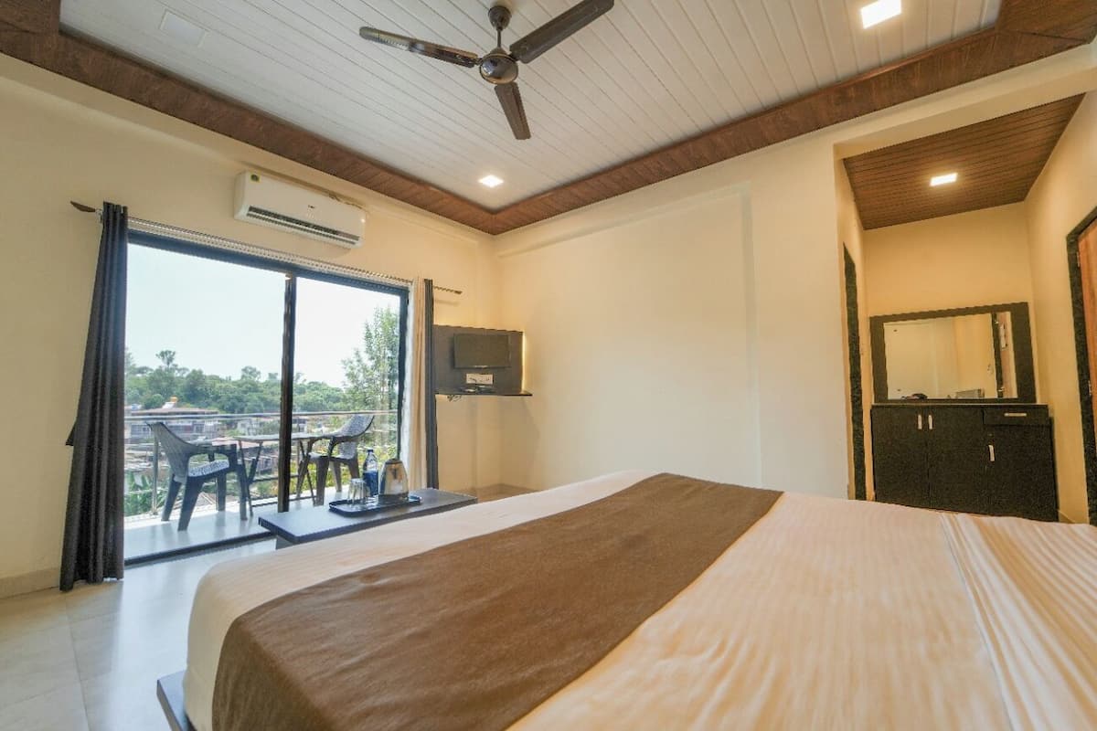 A hotel room with a bed, a ceiling fan, an air conditioning unit, a TV, a wardrobe, and a balcony with chairs and a table.