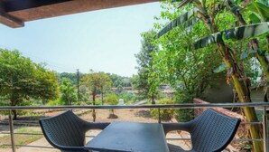 Un balcón con dos sillas y una mesa, con vistas a un paisaje verde con árboles y edificios.