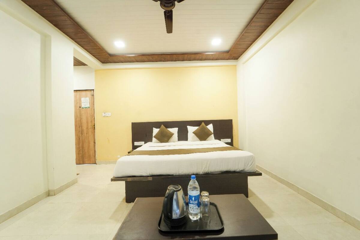 A hotel room with a bed, a tray with a kettle, a bottle of water, and a glass.