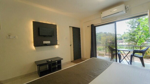 Habitación de hotel con una cama, un televisor montado en la pared, una mesita pequeña y un balcón con sillas.