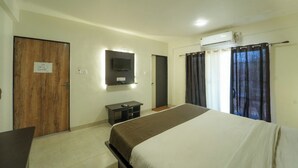 Habitación de hotel con cama, televisor montado en la pared, puerta de madera y ventana con cortinas.