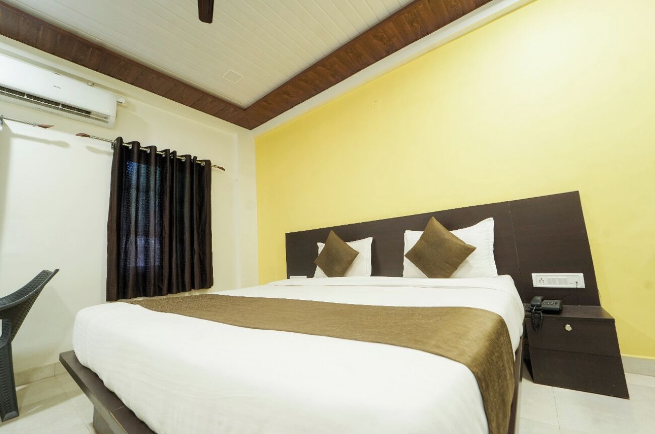 Una habitación de hotel con una cama, una mesita de noche, un equipo de aire acondicionado y una silla.