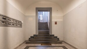 A staircase leading to a door with a metal gate, a tiled floor, and a wall-mounted storage unit with multiple compartments. - Joivy Piazza di Spagna apartment (Rome)