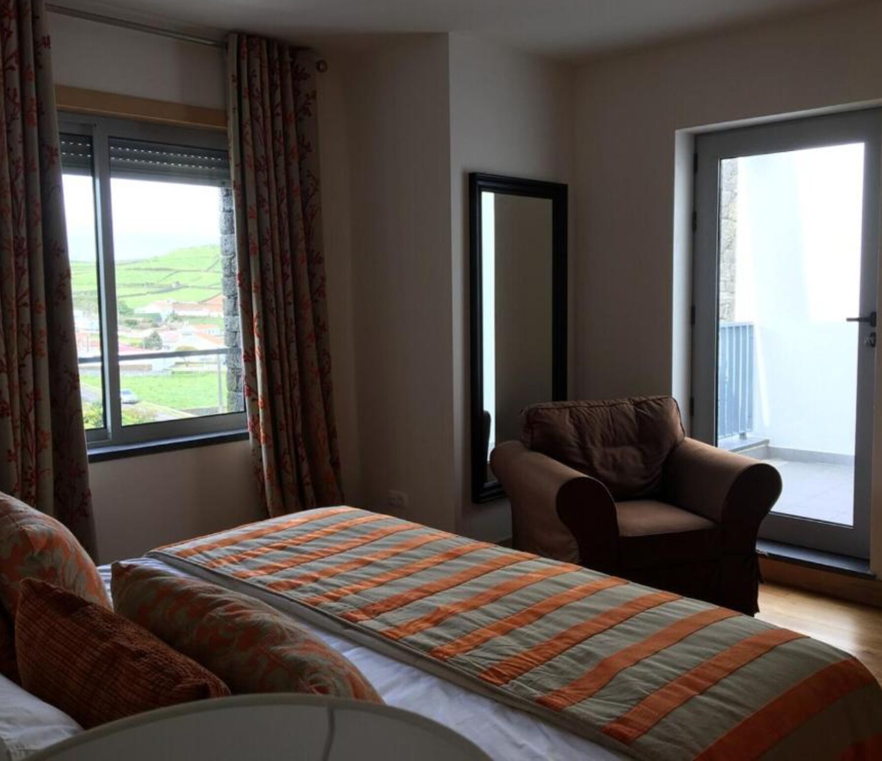 Una habitació d'hotel amb un llit, una cadira, una finestra gran i vista al camp.