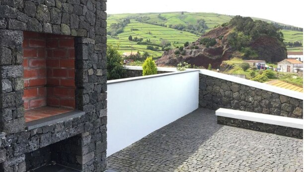 Un espacio al aire libre de piedra con chimenea de ladrillo, una pared blanca y suelo de adoquines.