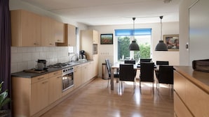 Una cocina moderna con armarios de madera, un comedor con sillas negras y vistas al exterior.