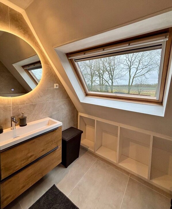 A modern bathroom with a skylight, a vanity with a mirror, and a small trash bin. - Spacious country house with a hot tub (Schoonloo)