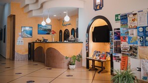 Ein Hotel-Empfangsbereich mit einer gebogenen Theke, einem Blumentopf und verschiedenen Informationsplakaten an den Wänden.