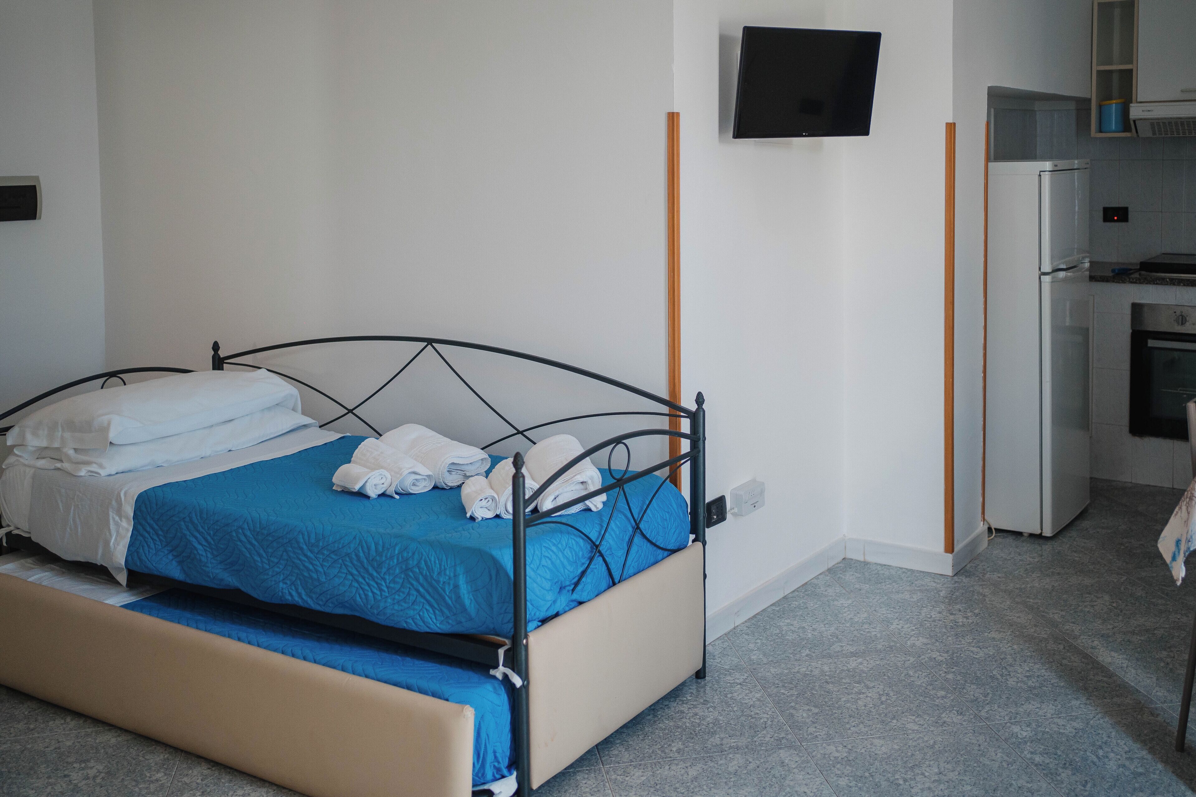 Een enkel bed met een blauw-witte dekbedovertrek, een klein nachtkastje en een aan de muur bevestigde televisie.
