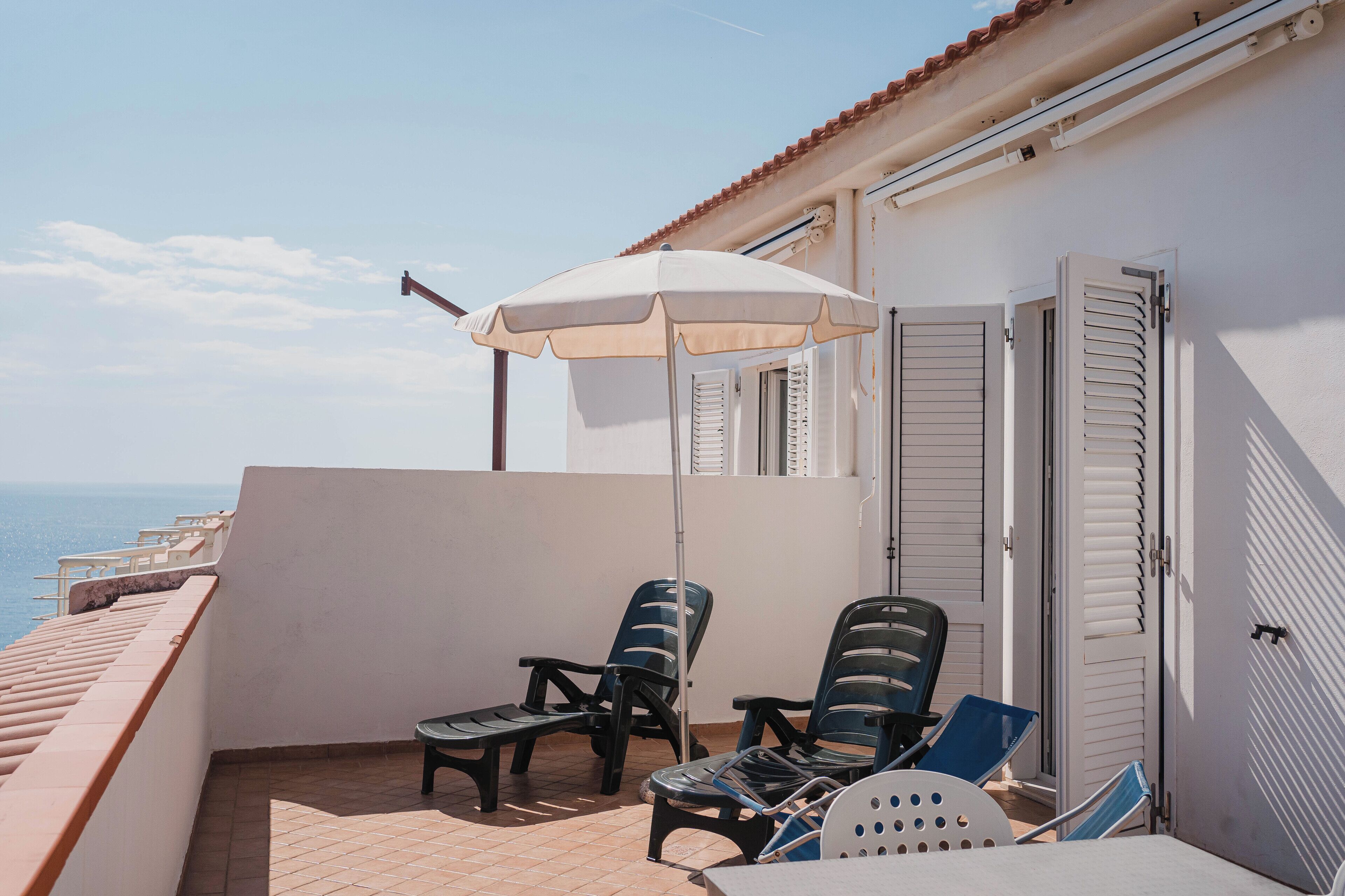 A balcony with two chairs, a table, and a white umbrella.