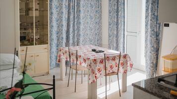 A dining area with a table set for four, surrounded by chairs, a cabinet with glass doors, and blue floral curtains.