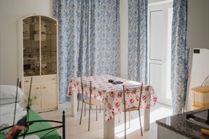 A dining area with a table set for four, surrounded by chairs, a cabinet with glass doors, and blue floral curtains.