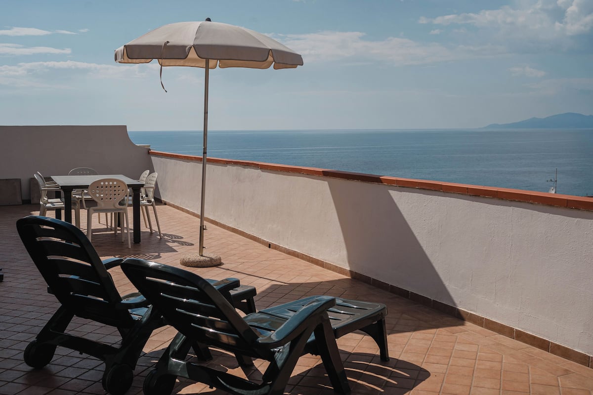 A balcony with a table, chairs, and an umbrella overlooking the sea.