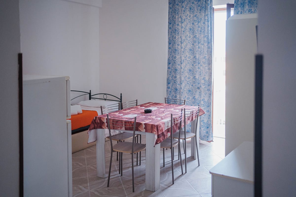 A small, clean room with a bed, a table with chairs, and a window with curtains.