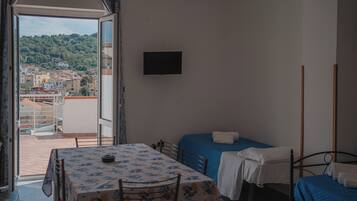 Una camera da letto con balcone, un letto, un tavolo con tovaglia floreale e una TV a parete.