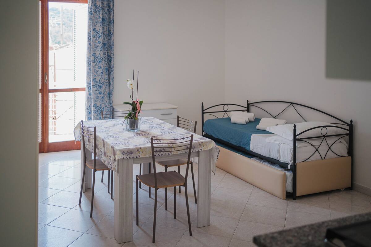 A bedroom with a bed, a bedside table, a chair, and a window with curtains.