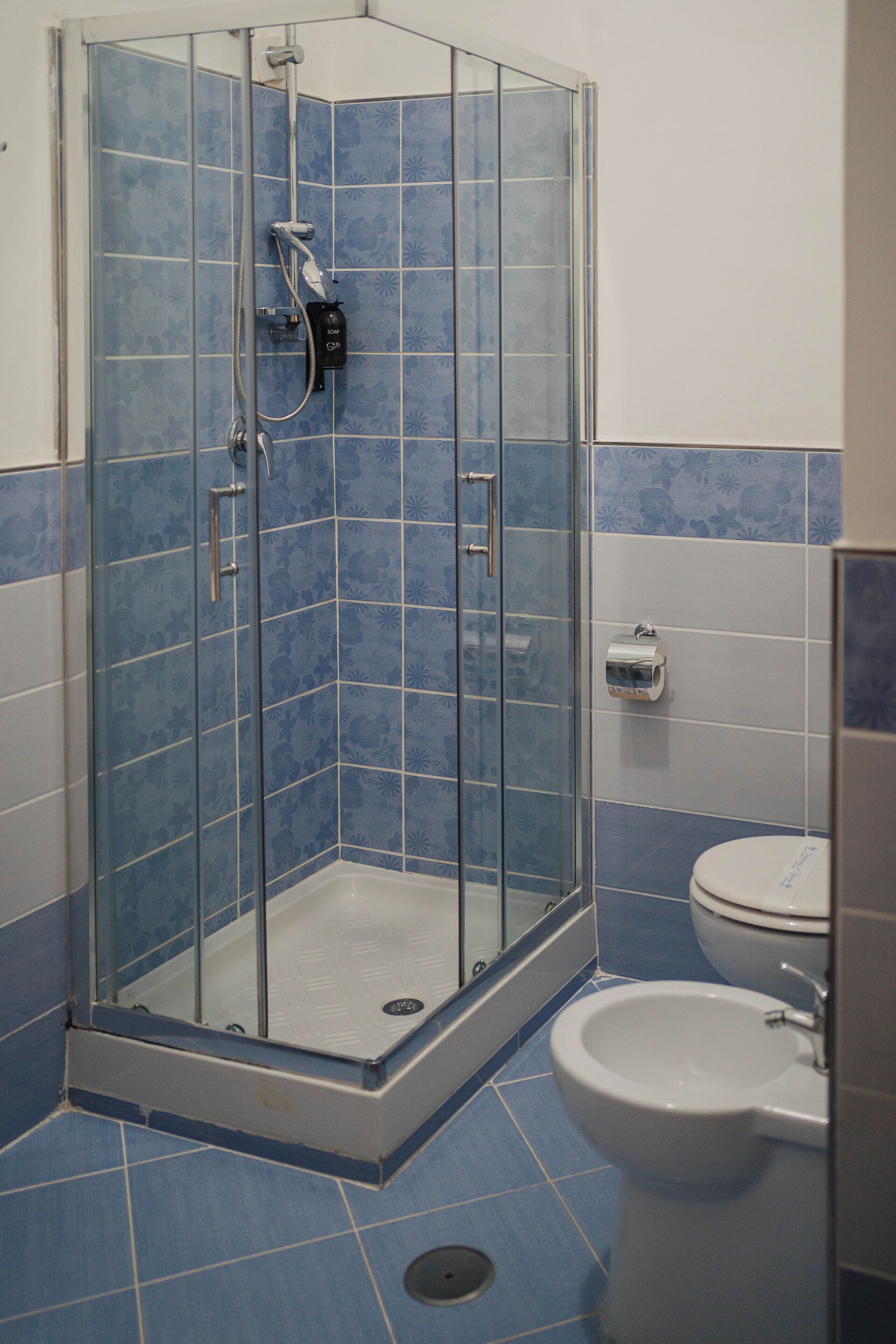 A shower with a glass door, a toilet, and blue-tiled walls.