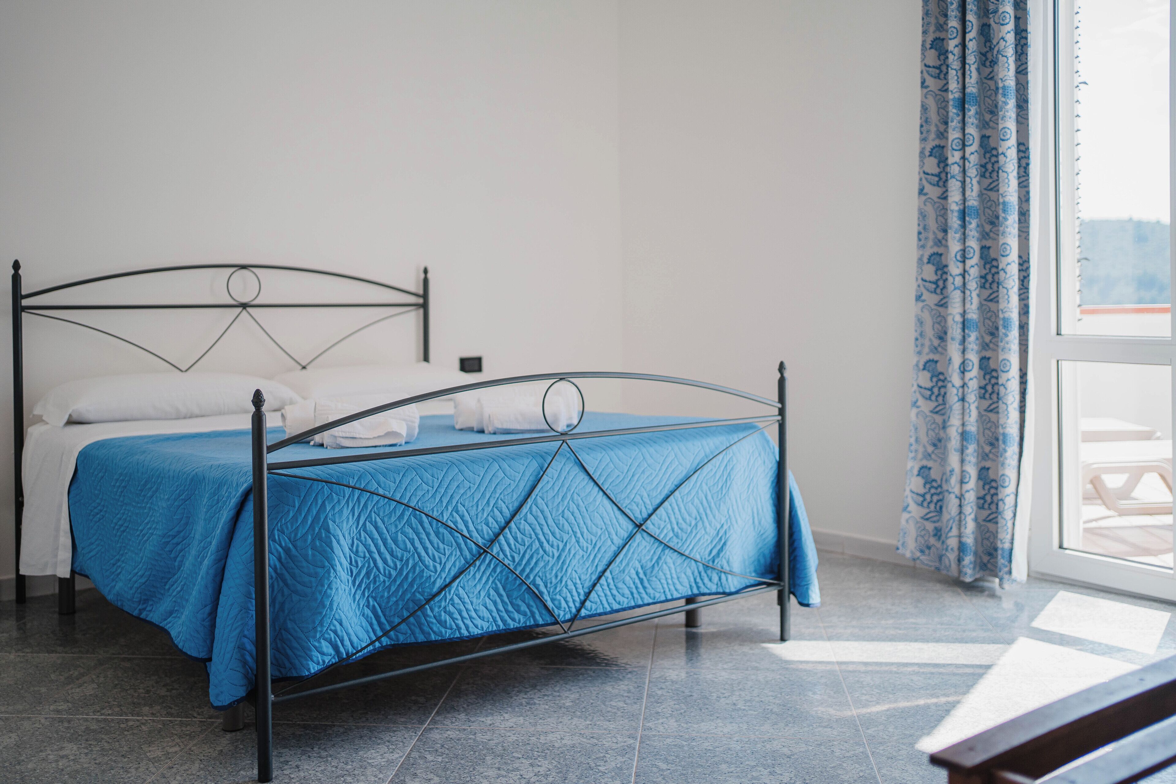 Un letto con copriletto blu, struttura in metallo e cuscini bianchi.