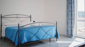 Un letto con copriletto blu, struttura in metallo e cuscini bianchi.