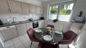 A modern kitchen with white cabinets, a dining table set for four, and a window with blinds.